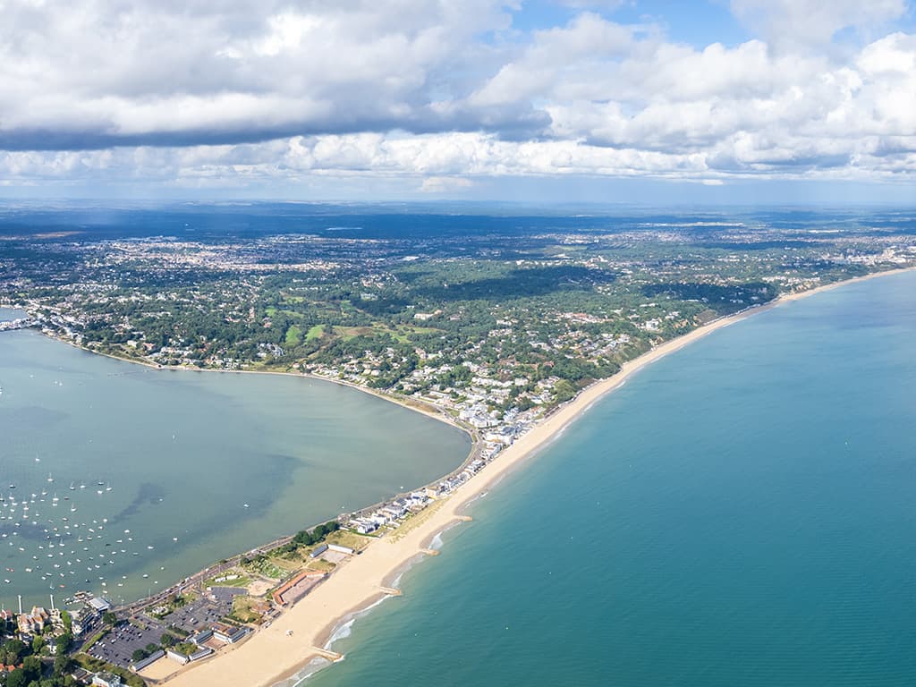 Aerial view of Sandbanks showing Poole Harbour with moored yachts on one side and the open sea along Sandbanks Beach on the other