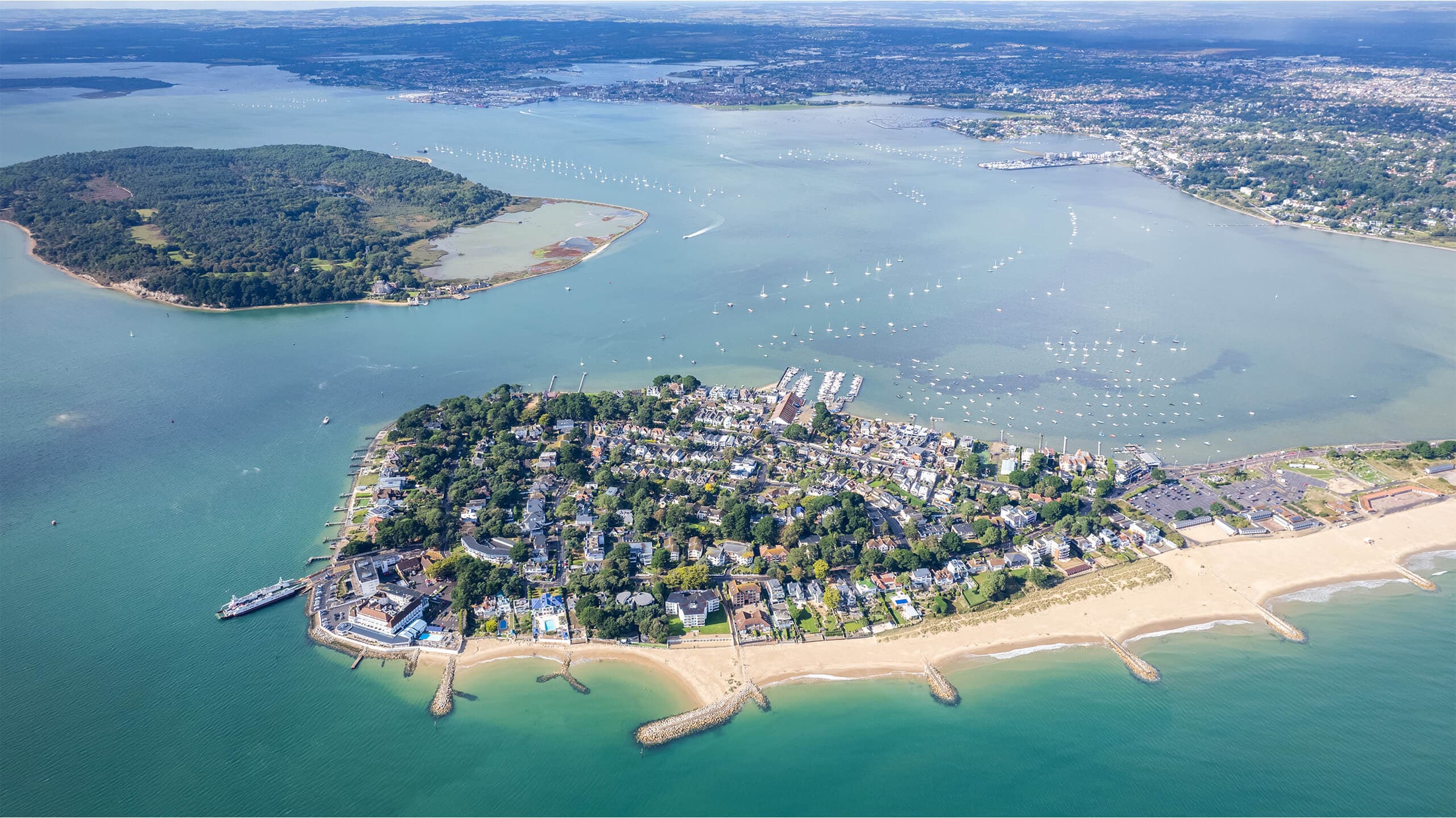Aerial wide-angle view of the Sandbanks Peninsula tip, with Sandbanks Beach, Poole Harbour and Brownsea Island on a sunny day